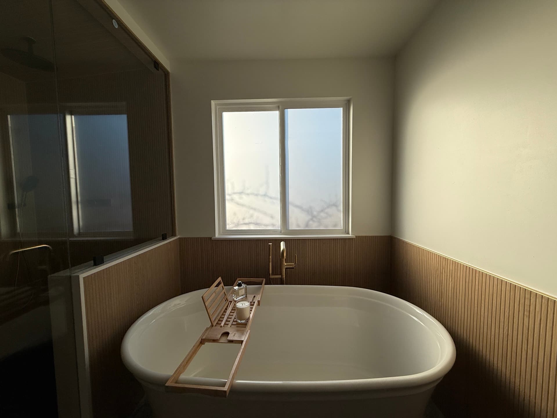 Freestanding soaking tub with brass filler under a wood-paneled wall in a Fair Oaks master bathroom