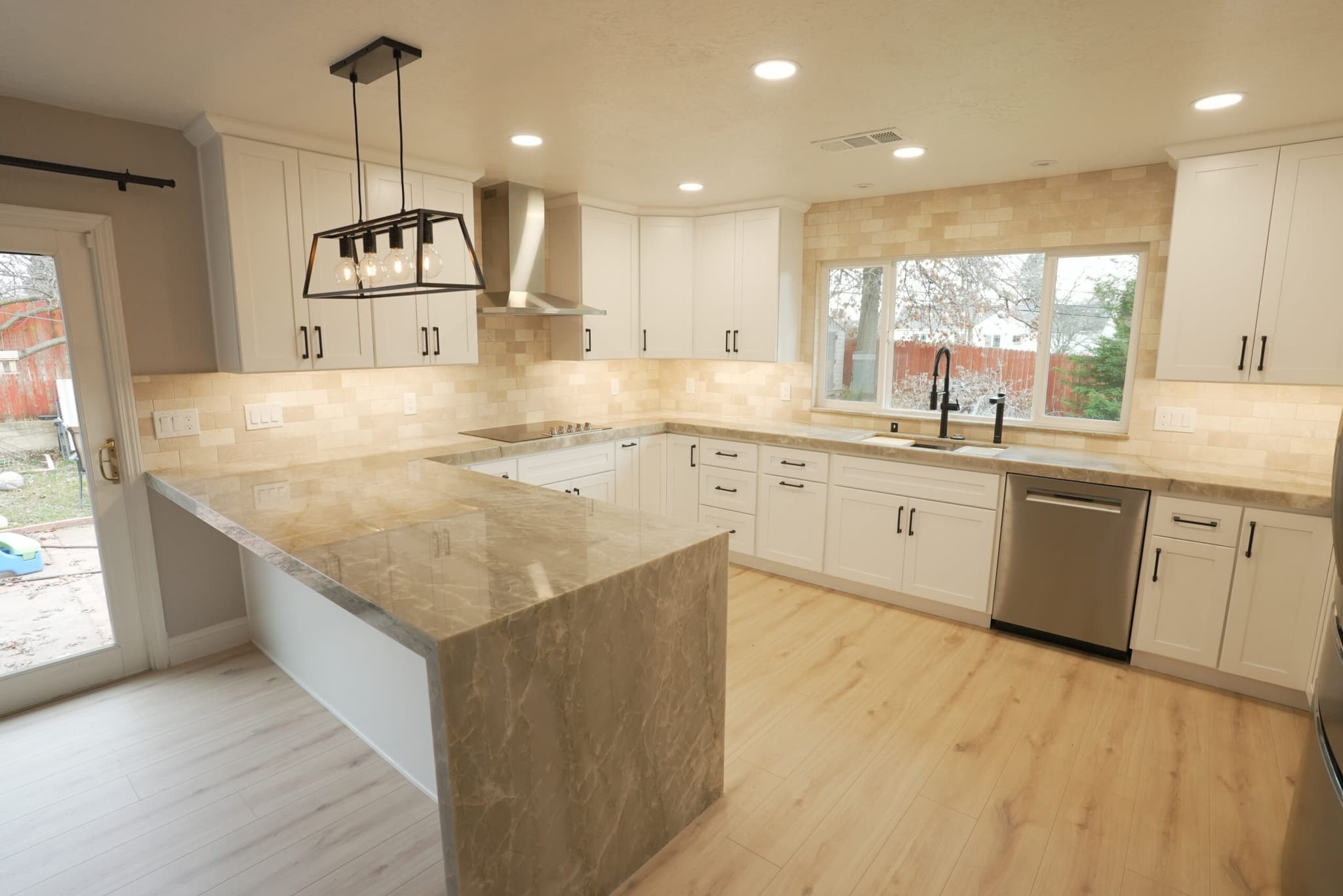 Wide-plank natural wood-look flooring running through a finished Fair Oaks kitchen with white cabinets and stone countertops
